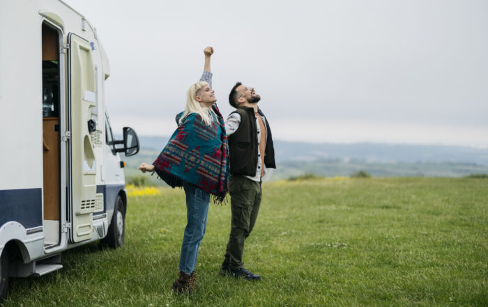 Happy tourists are raising their arms and breathing fresh air near their camper van, enjoying freedom and connection with nature during their road trip